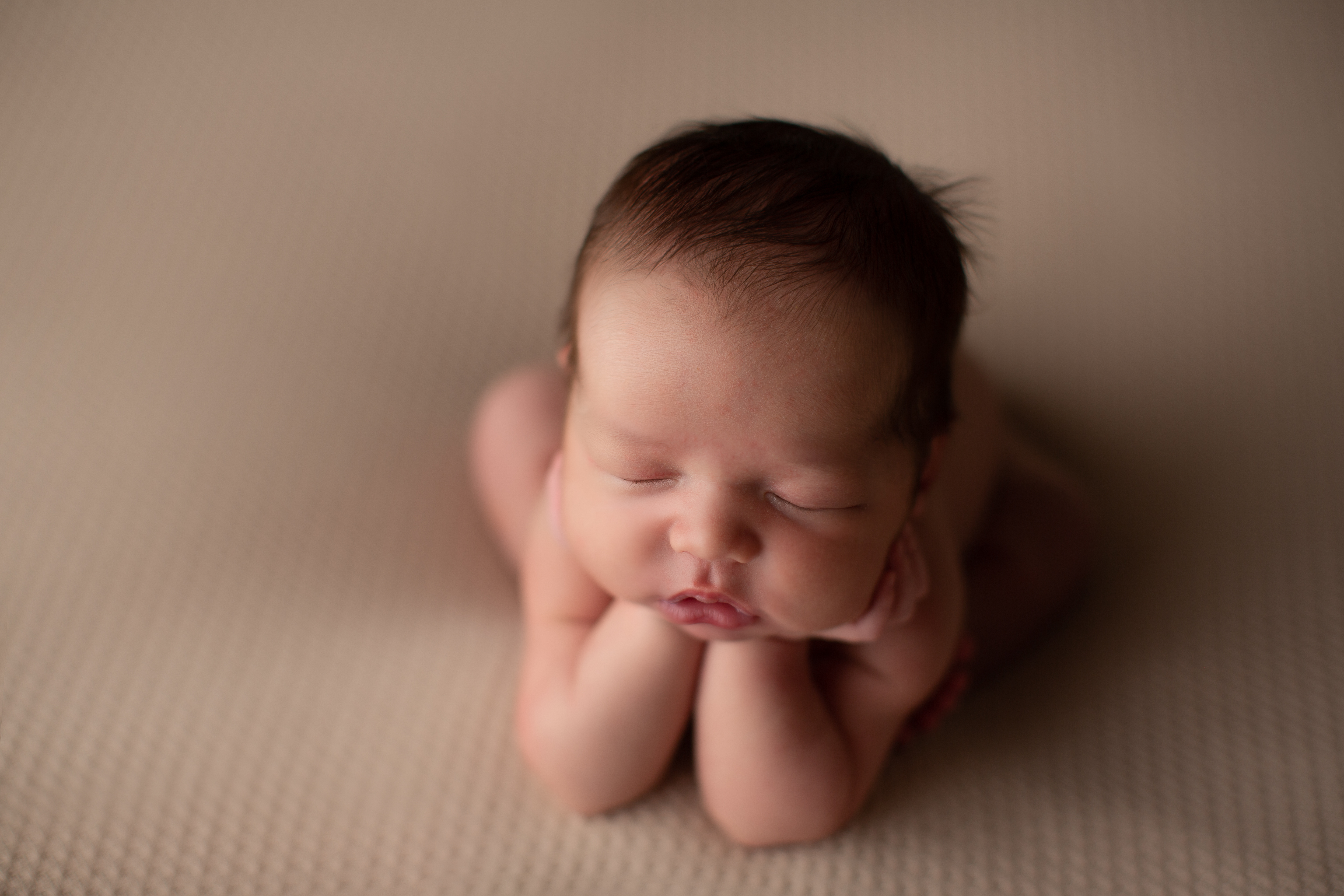 A newborn boy in the froggy pose on a neutral backdrop
